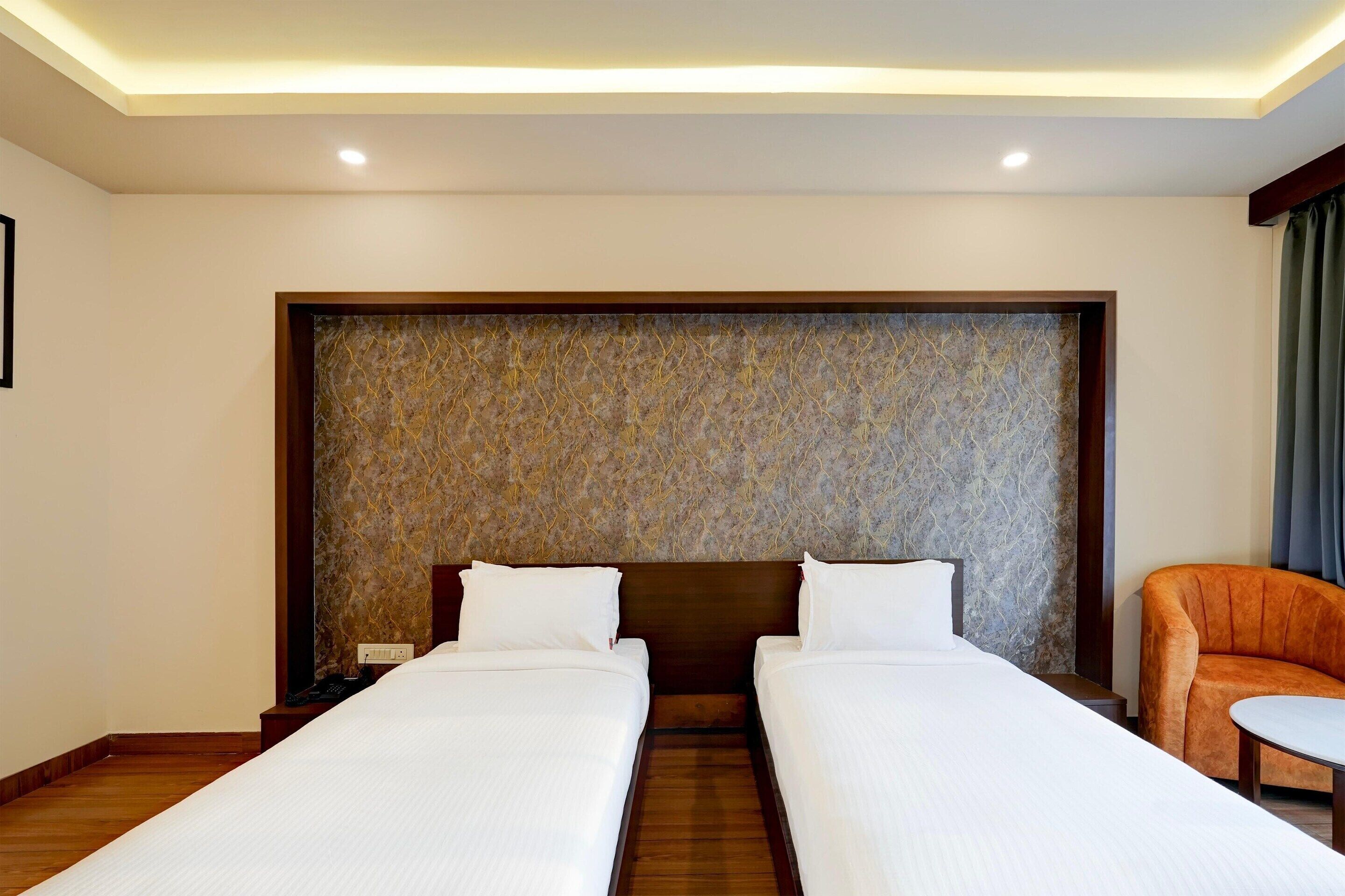 A hotel room with two single beds, a wooden headboard, a marble-patterned accent wall, and a small table with a chair.