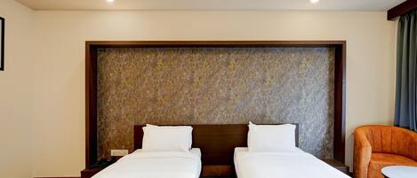 A hotel room with two single beds, a wooden headboard, a marble-patterned accent wall, and a small table with a chair.