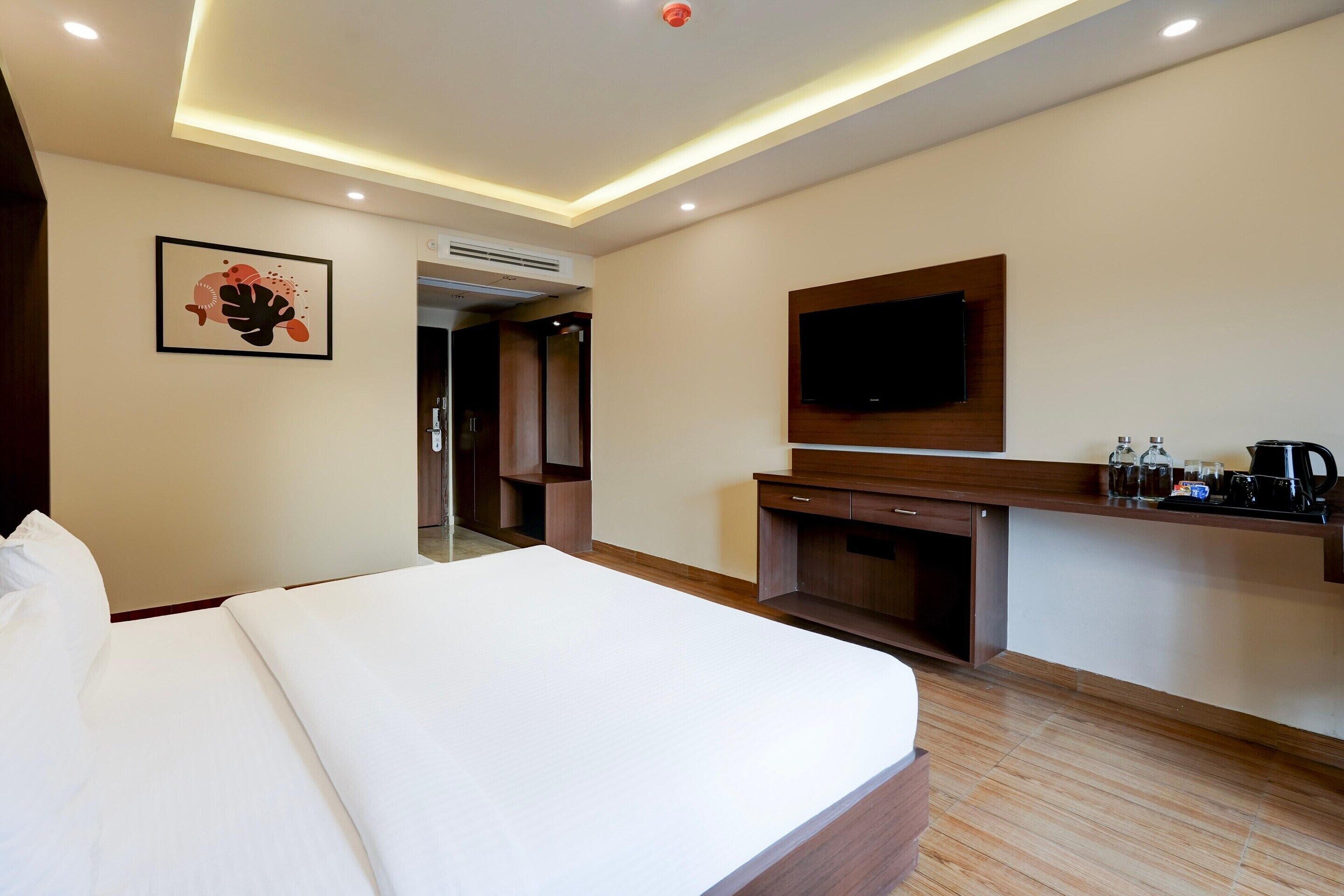 Ein Hotelzimmer mit einem großen Bett, einem flachbildfernseher an der Wand, einer kleinen Küchenzeile und einer Tür zu einem Badezimmer.