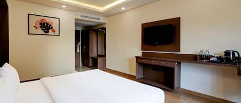 Ein Hotelzimmer mit einem großen Bett, einem flachbildfernseher an der Wand, einer kleinen Küchenzeile und einer Tür zu einem Badezimmer.