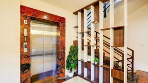 An elevator with a marble wall, a staircase with wooden railings, and a potted plant.