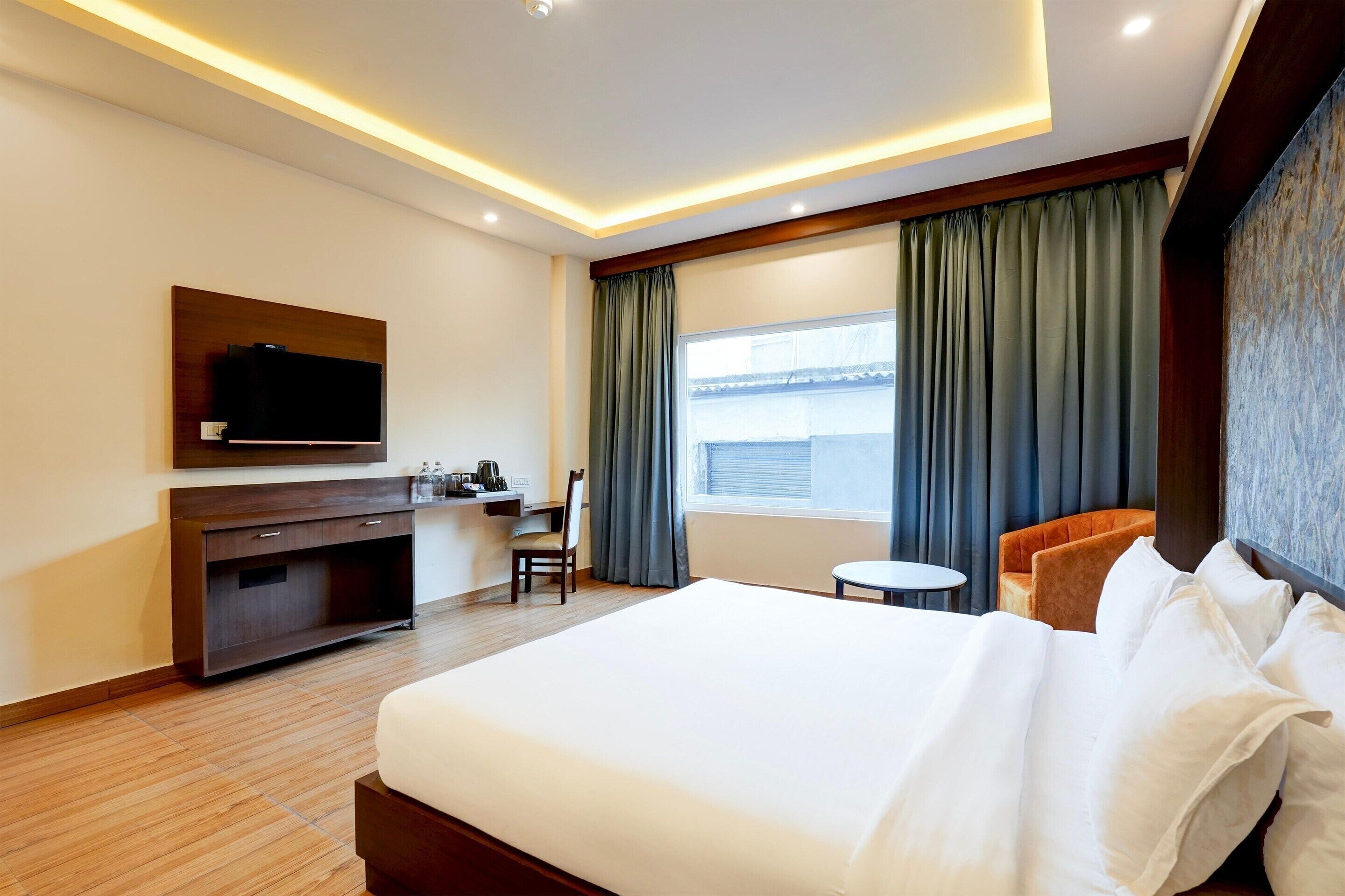A hotel room with a large bed, a desk with a chair, a television, and a window with curtains.