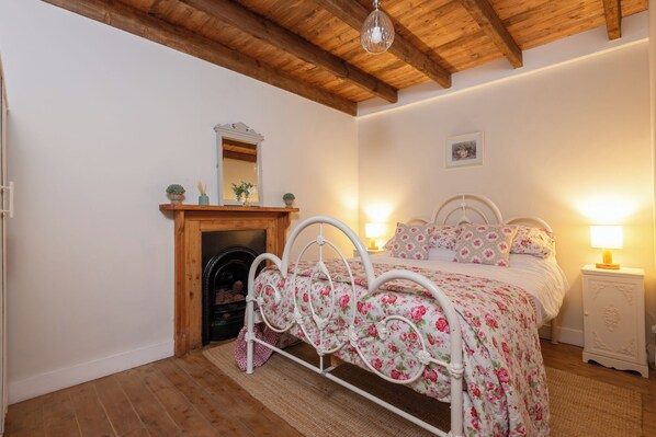 A bedroom with a wooden ceiling, a fireplace, a bed with floral bedding, and bedside lamps.