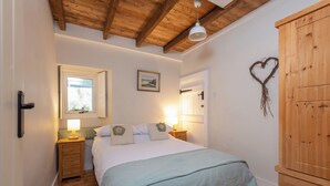 Une chambre avec un plafond en bois, un lit recouvert d’une couverture bleue, une table de chevet avec une lampe, une armoire en bois et un décor en forme de cœur accroché au mur.