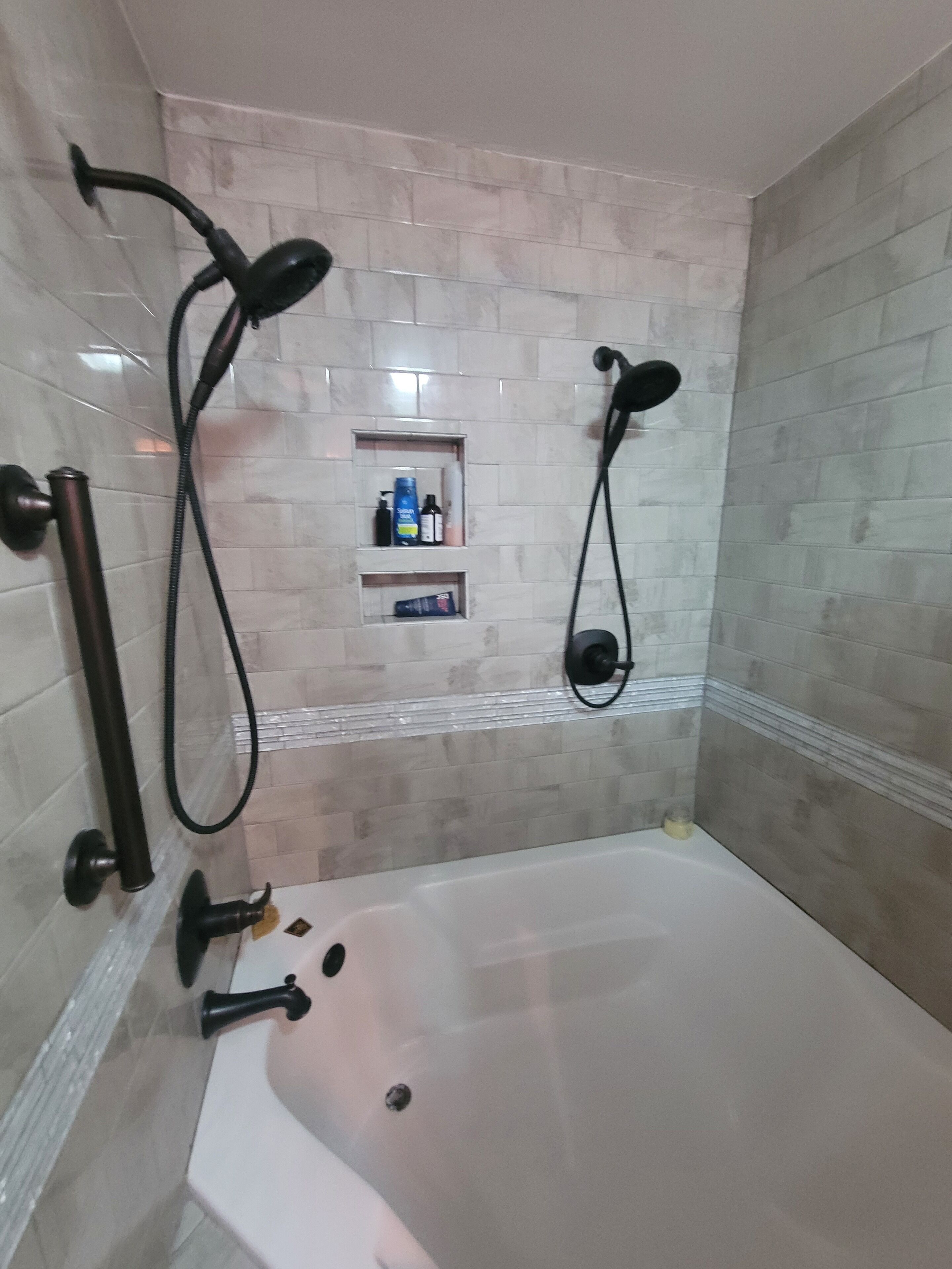 A bathroom with a bathtub, two showerheads, and two shelves with toiletries.