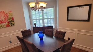 Une salle à manger avec une table en bois foncé, six chaises rembourrées, un vase bleu et un lustre.