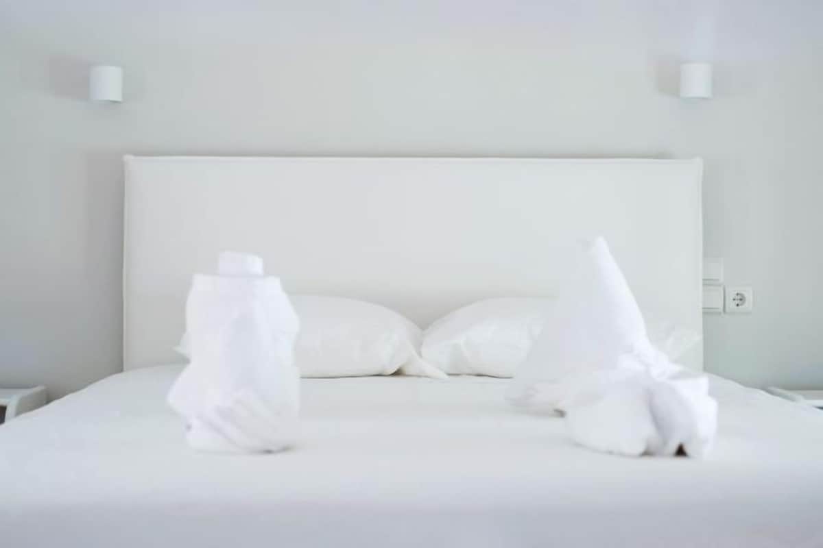 A hotel room with a large bed, white linens, and two wall-mounted light fixtures.