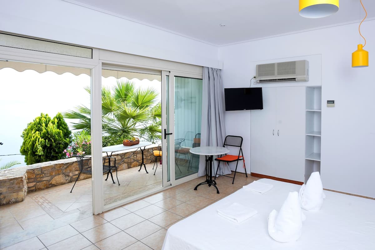 A hotel room with a balcony, a bed with white linens, a TV mounted on the wall, and a small table with chairs.