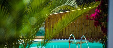 Una terraza de madera con piscina, rodeada de vegetación y una valla de madera.