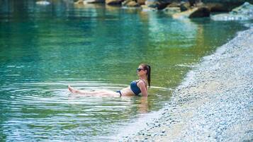 A person in a swimsuit floating in clear water near a pebble beach.