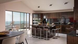 A modern kitchen with a central island, bar stools, and a large window overlooking a balcony.