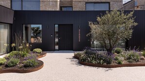 A modern building with a dark facade, a visible entrance, and a landscaped garden with various plants and flowers.