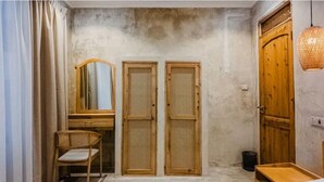 A room with a wooden desk, a chair, two doors with mesh screens, a mirror, a hanging light fixture, and a wooden cabinet.