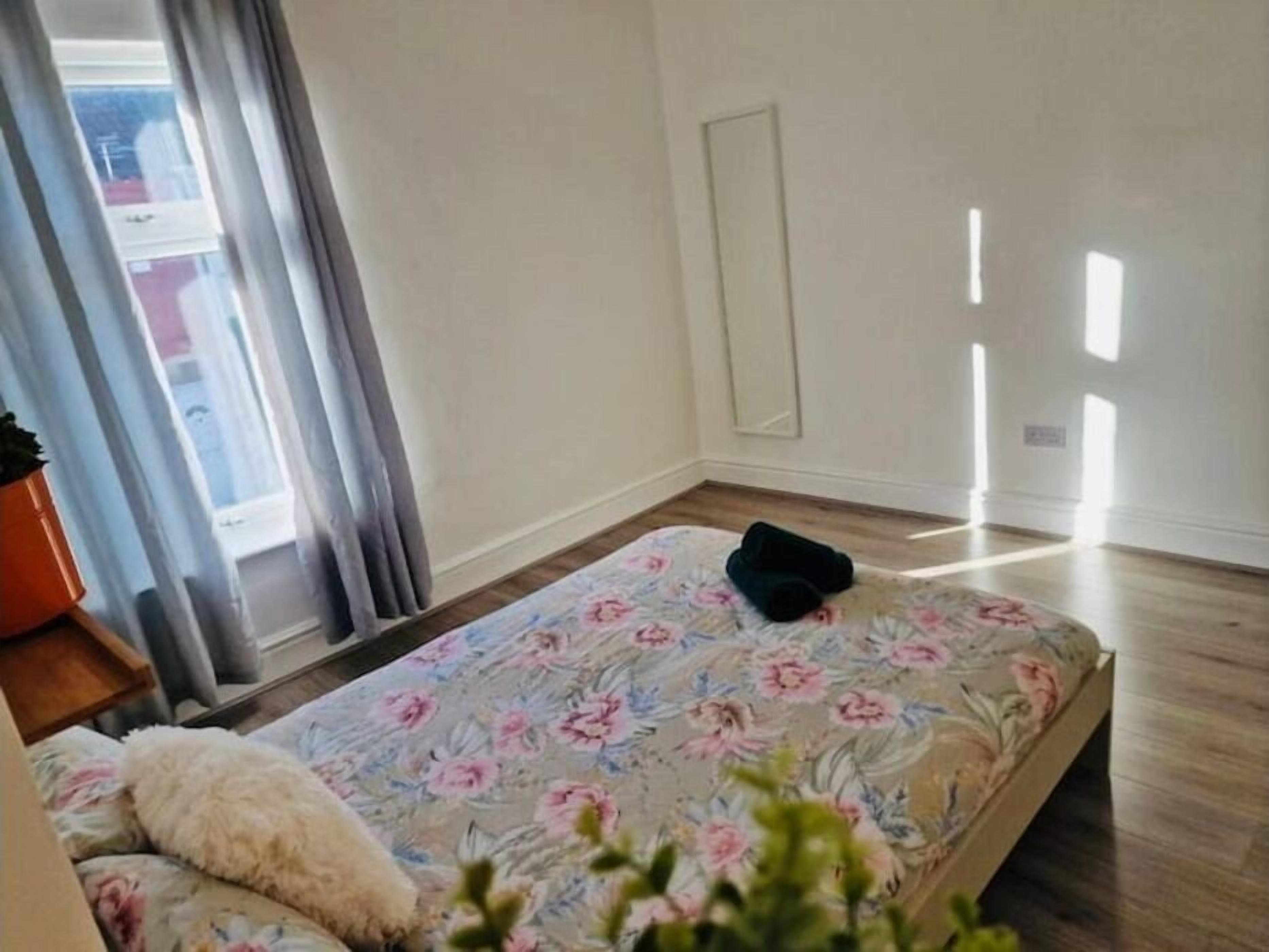 Un dormitorio con colcha estampada, almohada mullida blanca y un objeto negro pequeño sobre la cama, además de suelo de madera.