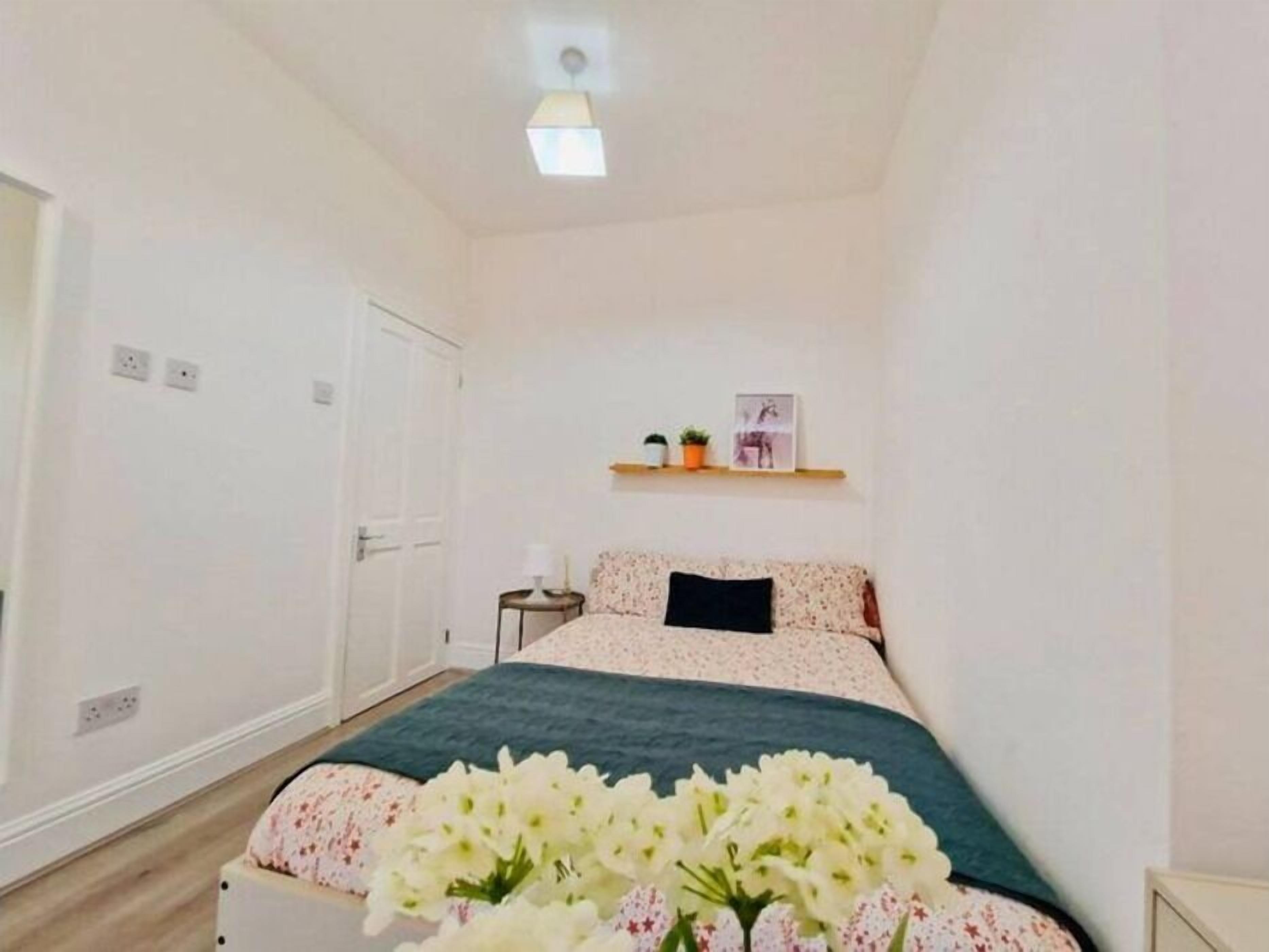 Une chambre à coucher comprenant un lit, une table de chevet, une commode, une étagère avec des objets décoratifs et une fenêtre.