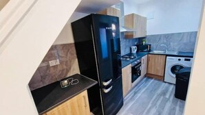 Una cocina moderna con un refrigerador negro, armarios de madera, horno integrado y lavadora.