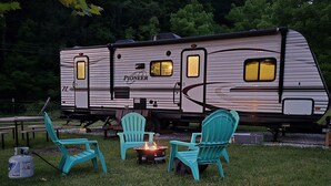 A Pioneer RV with a fire pit and two turquoise Adirondack chairs in a grassy area.