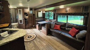 A compact RV interior with a kitchenette, a dining area, and a seating area with a sofa and cushions.