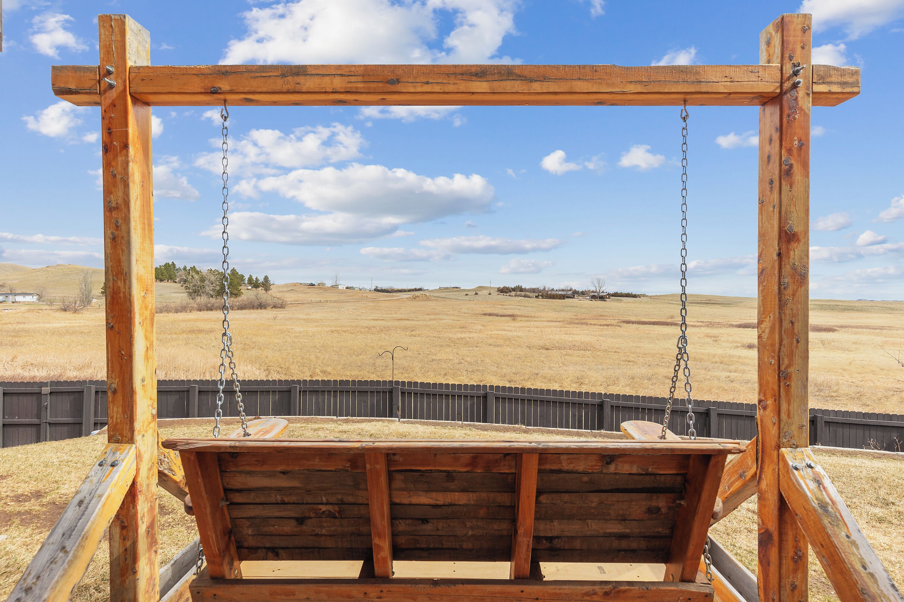 Eine Holzschaukel auf einem freien Feld, bewölkter Himmel.
