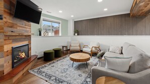 A modern living room with a fireplace, a flat-screen TV, and a comfortable seating area with a sofa and chairs.