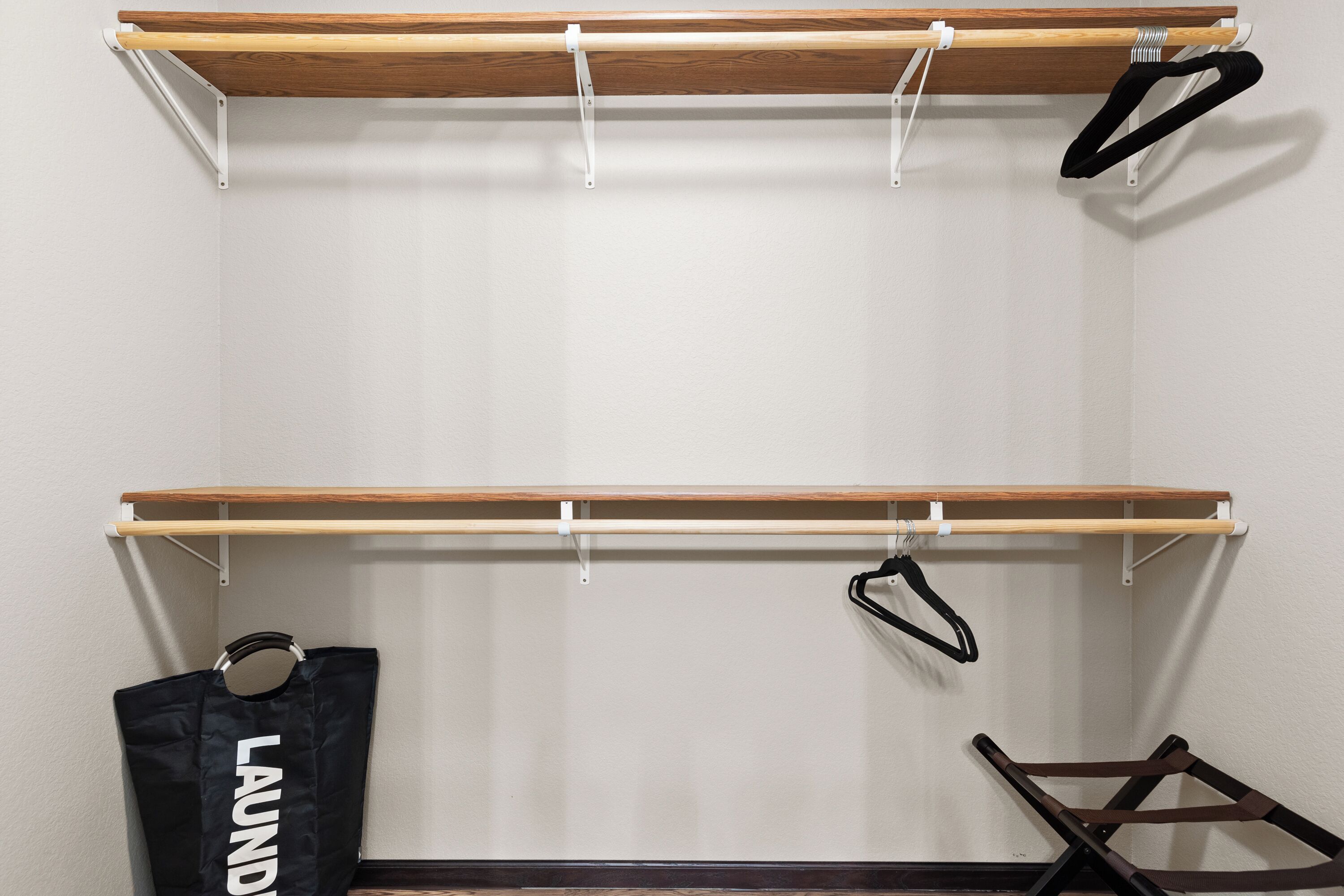 A room with two wooden shelves, one above the other, with a black hanger on the top shelf and a black bag with "LAUNDRY" on it hanging on the bottom shelf.