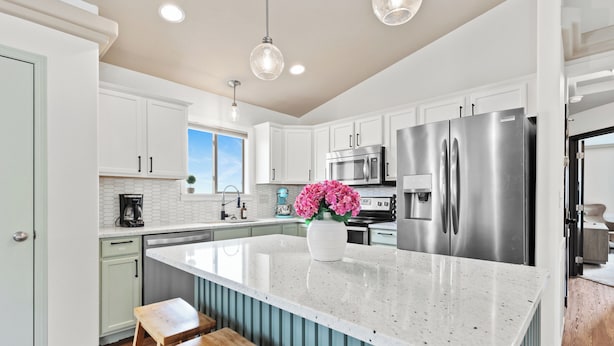 A modern kitchen with white cabinets, stainless steel appliances, a large island with stools, and a view to the outside.