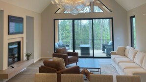 A spacious living area with a modern chandelier, a fireplace, and a large dining table. - Brand NEW MINT Windham 5BR/4.5BA home on 5 acre, wooded hilltop. (Windham)