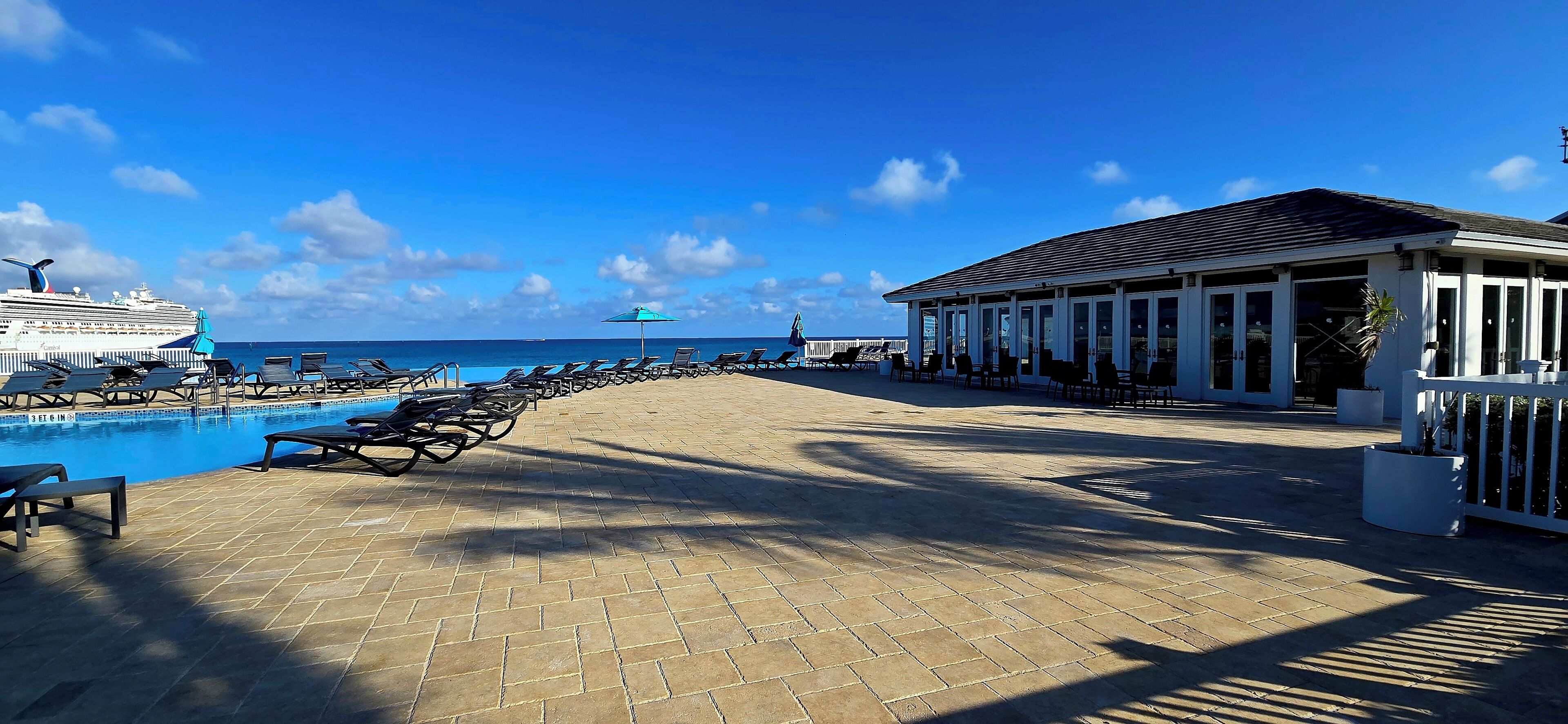 A beachside pool area with lounge chairs and a building with large windows.