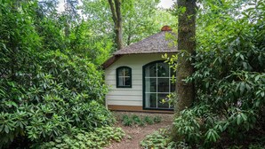 Una pequeña casa rodeada de abundante vegetación, con un sendero de tierra que lleva a la entrada.