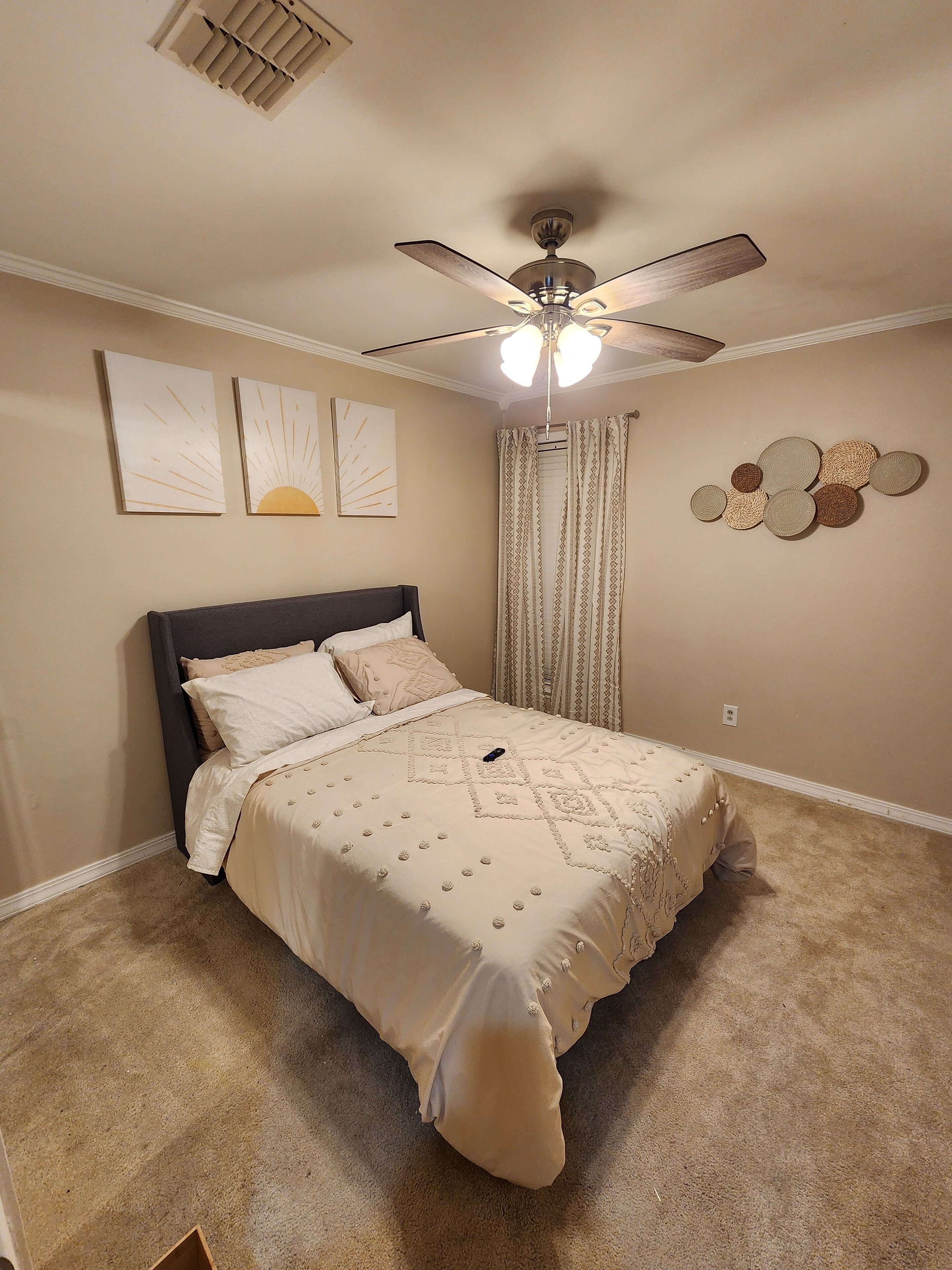 Une chambre à coucher avec un lit, un ventilateur de plafond, des œuvres d’art et des rideaux.
