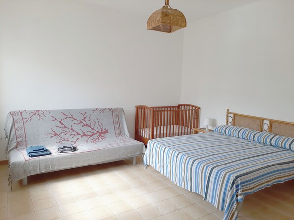 A room with a bed, a wooden crib, a sofa, and a hanging light fixture. - Villa Solento (Crab House): with all the comforts just a stone's throw from the sea. (Campomarino)