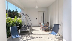 Un balcón con una silla mecedora, una mesa de comedor con sillas, y una silla plegable azul.