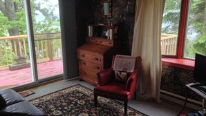 Una habitación con una silla roja, un aparador de madera, un televisor y un ventanal con vistas a un balcón.