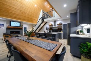 Eine moderne Küche mit dunklen Schränken, einer Holztreppe und einem Essbereich mit einem langen Tisch und Stühlen.