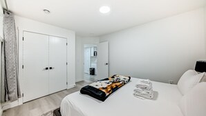 A hotel room with a bed, a bedside table, a lamp, a wardrobe, and a bathroom visible in the background. - Rome Sweet Home 2. Private Guest Suite in a quiet, family-friendly neighborhood. (Calgary)