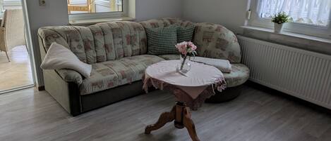 A living room with a sofa, a small table with a vase of flowers, and a window with curtains.