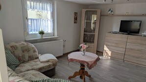 Una sala de estar con un sofá, una mesita redonda con un florero, un televisor y un aparador.