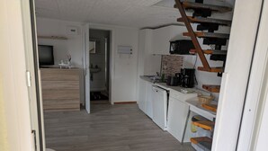 Cocina moderna con armarios blancos, lavavajillas y cafetera. Se ve una escalera de madera con barandilla metálica que conduce a otra habitación.