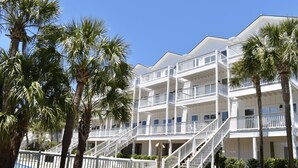 Een meerhoog hotel met balkons, palmbomen en een helderblauwe lucht.
