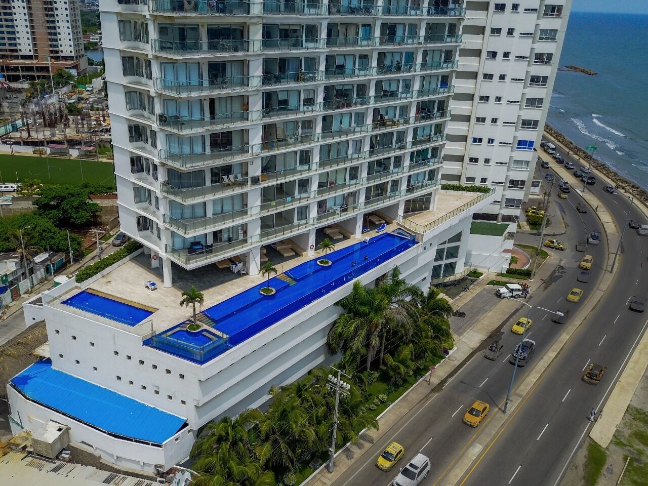 A high-rise hotel with multiple balconies, a rooftop pool, and a view of the ocean.