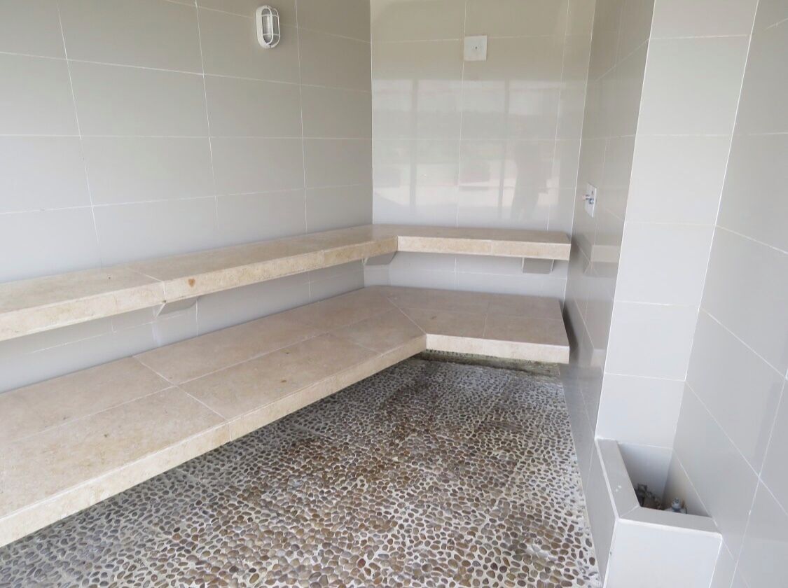 A bathroom with a tiled floor, a shower area, and a shelf.