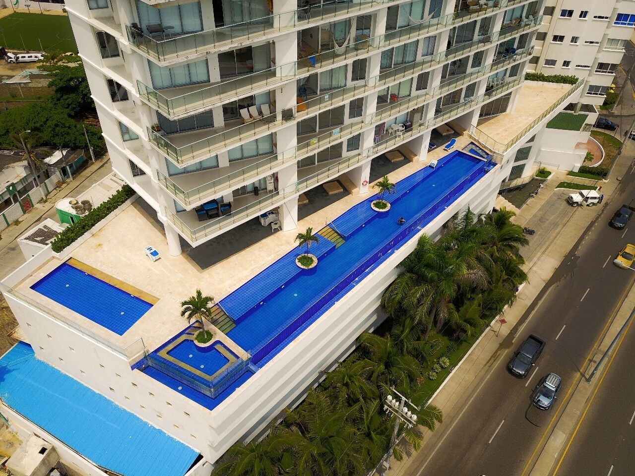 Un hotel de diverses plantes amb una zona de piscina al terrat, balcons i vista al carrer.