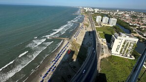 An aerial view of a coastal city with a beach lined with blue umbrellas, a road parallel to the shore, and high-rise buildings. - Charming 2-bedroom apartment in front of the Beach with WiFi, AC, Pool, Jacuzzi (Cartagena de Indias)