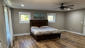 A bedroom with a wooden floor, a bed with a headboard, two windows, and a ceiling fan. - Charming 2-bedroom barn with WiFi, AC in awesome Midland (Midland)