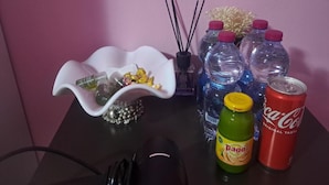 Una mesa con un tazón decorativo blanco, una botella verde etiquetada 'Pago', una lata roja de Coca-Cola y varias botellas de agua.