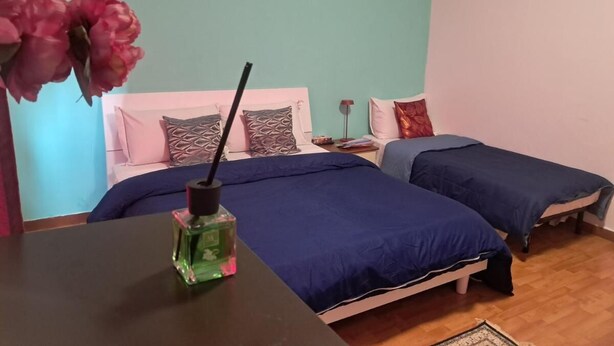 Un dormitorio con dos camas, una mesita de noche, una lámpara y una botella de perfume sobre una mesa.