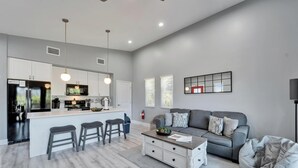 A modern kitchen with white cabinets, a central island with stools, and a grey sofa in the living area. - Relax & Recharge at 3BR Indian Rocks Beach Family Retreat - Short walk to beach (Indian Rocks Beach)