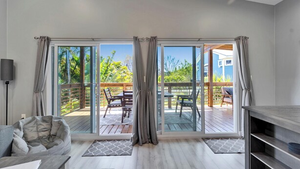 A room with a sliding glass door leading to an outdoor deck, a grey bean bag chair, a small table, and a TV stand. - Relax & Recharge at 3BR Indian Rocks Beach Family Retreat - Short walk to beach (Indian Rocks Beach)