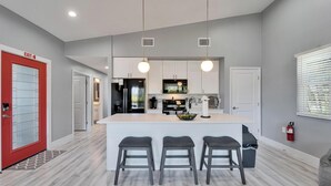 A modern kitchen with a central island, bar stools, and pendant lighting. - Relax & Recharge at 3BR Indian Rocks Beach Family Retreat - Short walk to beach (Indian Rocks Beach)