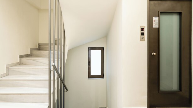 A staircase with a glass railing, a door with a frosted glass panel, and a small window. - Elysee apartment 7 (Athens)